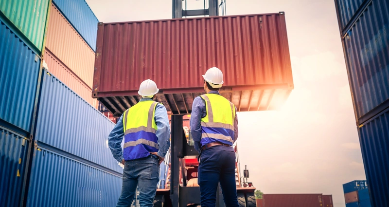 Zwei Arbeiter stehen vor einem Container der angehoben wird